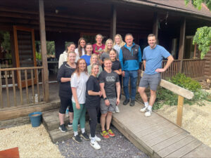 a group photo of the team outside the log cabin on their team building day 2023